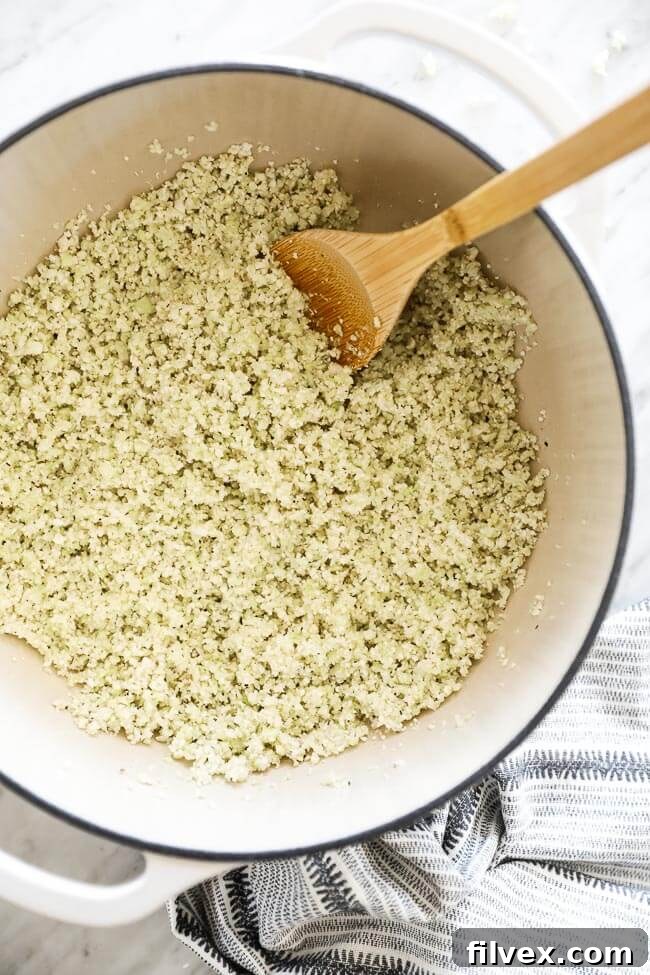 Vertical overhead image of cauliflower rice in a Dutch oven or covered baking dish, prepared for baking.
