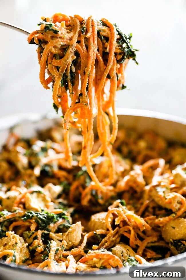 Large forkful of creamy chicken sweet potato noodles being lifted from a pan, showing the rich sauce and perfectly cooked noodles
