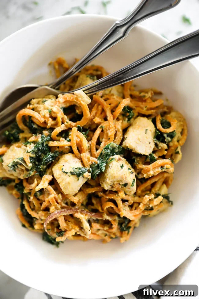 Overhead shot of creamy chicken sweet potato noodles in a white bowl with a fork and spoon, emphasizing its inviting texture