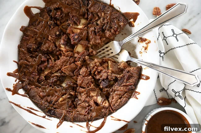 Gluten-free apple cake in a pie dish with a piece taken out and two forks dug. Caramel sauce drizzled all over the top.  