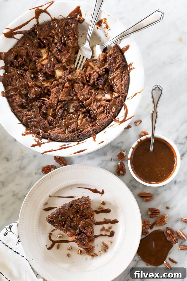 Gluten-free apple cake in a pie dish with a piece removed and served up on a plate. Caramel sauce drizzled all over the top with extra on the side. 