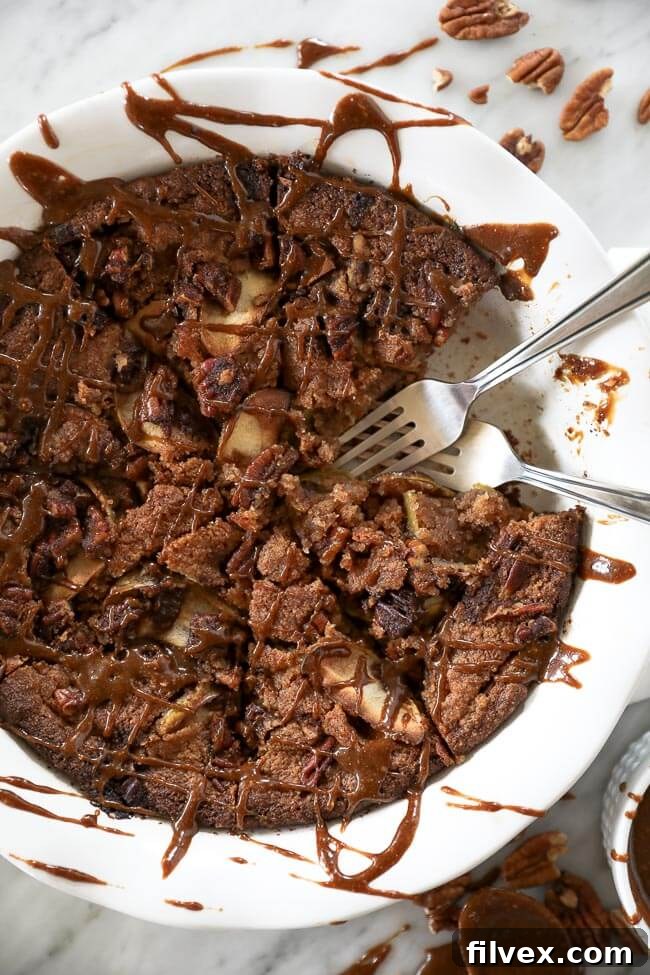 Close up of gluten-free apple cake in a pie dish with piece removed and two forks dug in. Caramel sauce drizzled all over top. 