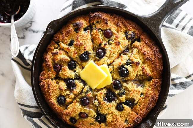 Horizontal overhead image of blueberry cornbread in a cast iron skillet with grass fed butter melting on top. 