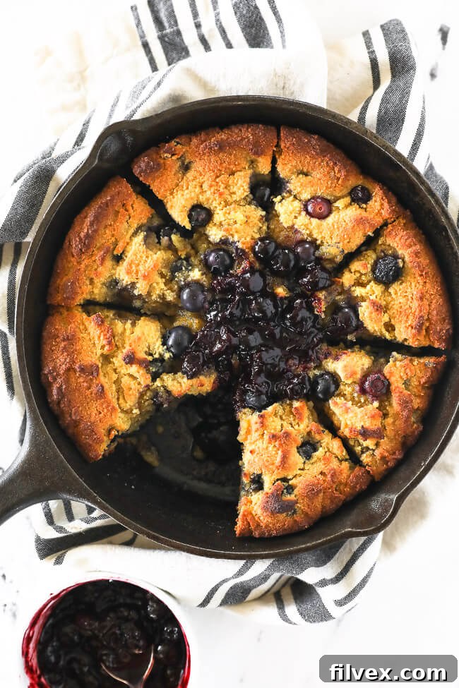 Vertical overhead image of gluten free and paleo cornbread in a skillet with blueberry sauce on top. 