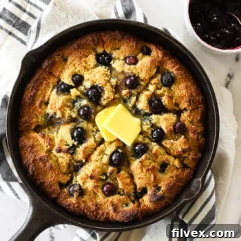 Blueberry cornbread in a skillet with blueberry sauce on the side and grass fed butter melting on top.