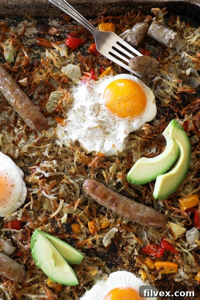 Close up image of sheet pan breakfast bake. Bake consists of hash browns, bell pepper, onion, sausages, eggs and topped with avocado. 