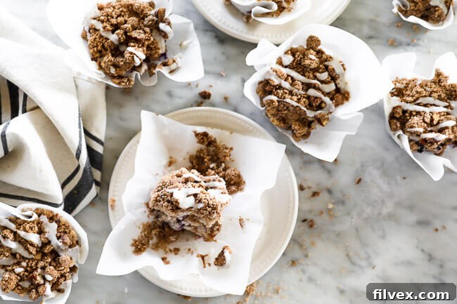 A beautiful spread of Paleo, Gluten-Free Coffee Cake Muffins on a marble surface, some on plates, all generously drizzled with coconut butter. 