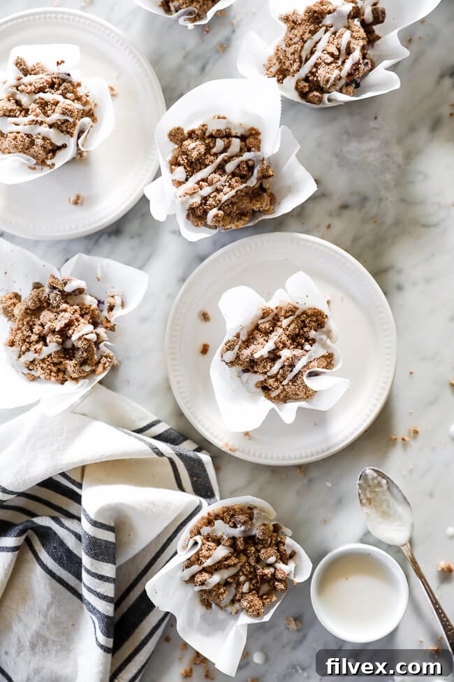 An inviting overhead vertical shot of coffee cake muffins scattered on a marble surface, with some elegantly placed on small white plates. A small bowl of extra coconut butter sits on the side with a spoon. 