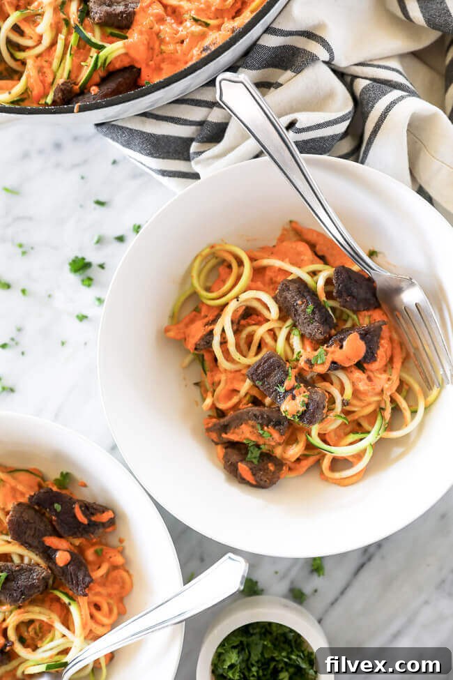 Overhead shot of roasted red pepper zoodle pasta with steak bits in a bowl with a fork, ready to be enjoyed.