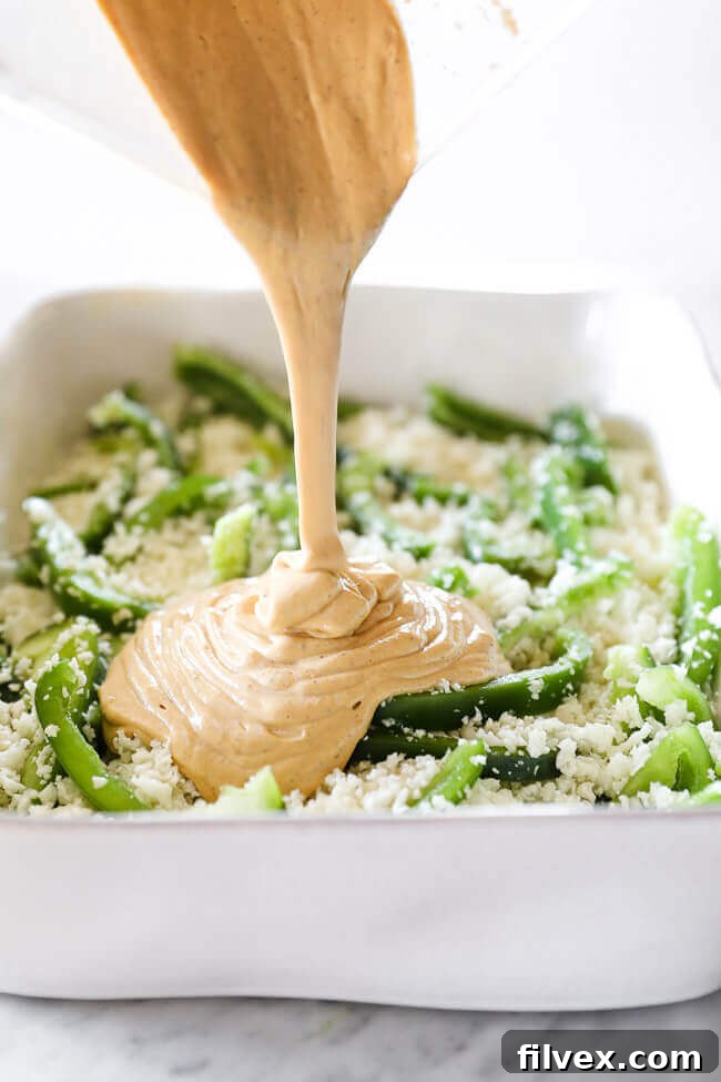 Creamy, smoky sauce being poured generously over a bed of vibrant cauliflower rice and thinly sliced bell peppers in a baking dish, preparing for a comforting Italian Sausage Casserole.
