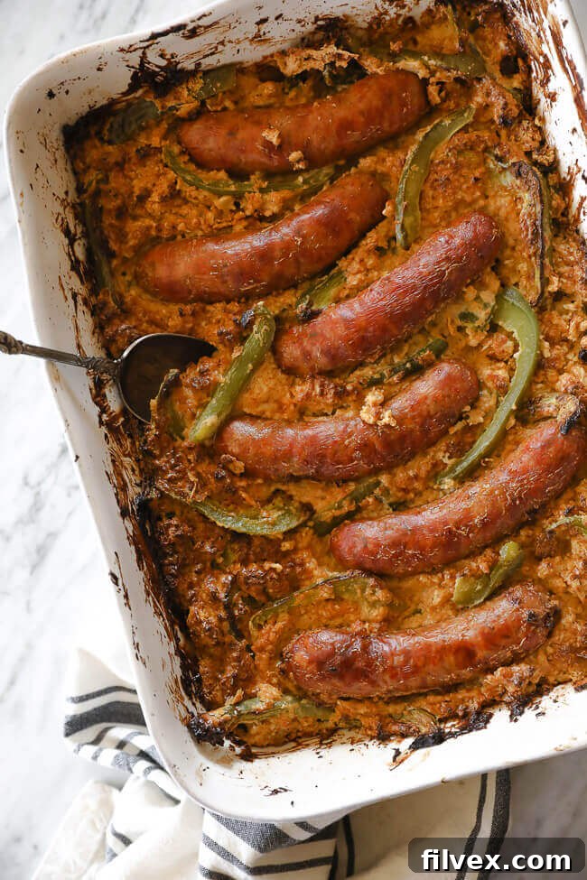 Succulent Italian sausages and vibrant bell pepper strips beautifully arranged over a bed of creamy cauliflower rice in a casserole dish, ready for baking. An inviting overhead vertical shot.