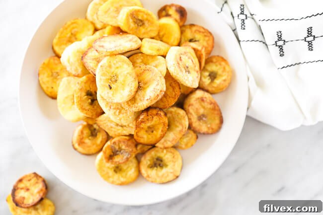 Horizontal overhead image of perfectly golden pan fried green plantains piled up on a white plate, ready to be served.