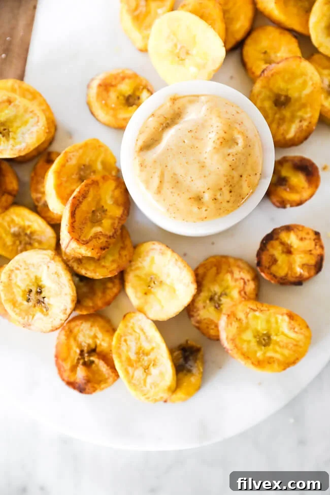 Close up vertical overhead image of glistening pan fried plantains, perfectly cooked, with a small bowl of savory dipping sauce positioned beside them.