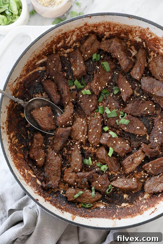 Close-up of Korean beef bulgogi cooking in a pan with a spoon, highlighting the rich sauce