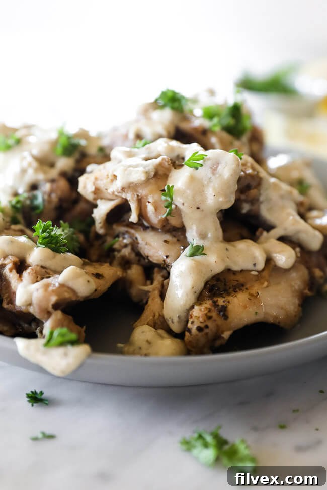 Chicken thighs stacked up on a plate and covered in creamy sauce topped with chopped parsley close up straight on vertical image 