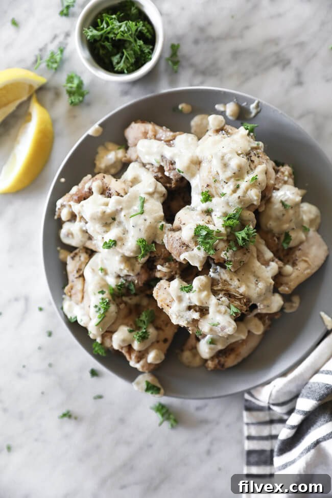 Chicken thighs covered in creamy sauce on a plate with lemon wedges vertical overhead image