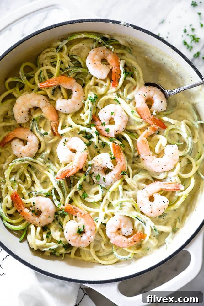 Vertical image of creamy garlic shrimp in a skillet with a serving spoon. Parsley sprinkled on top. 