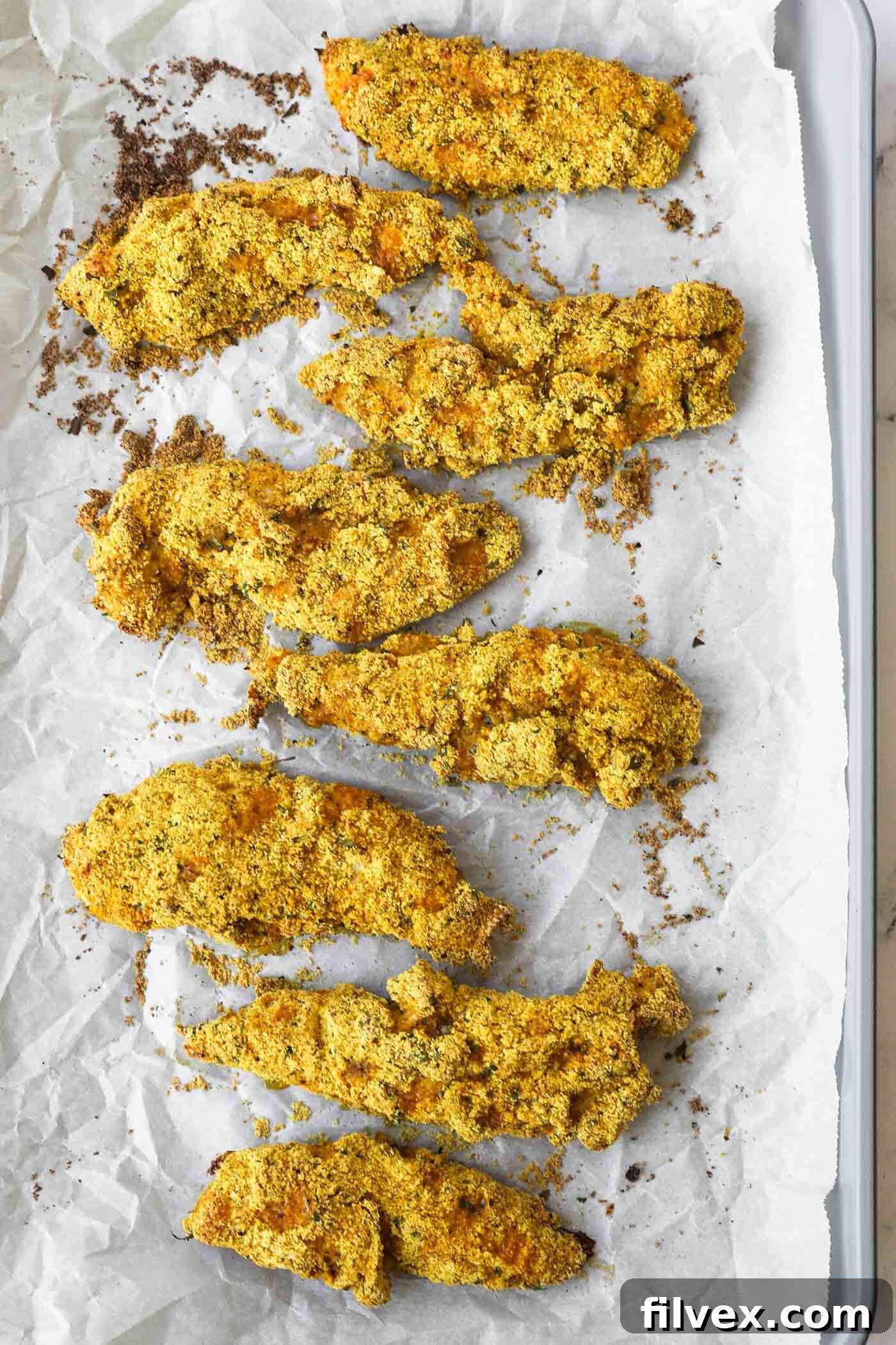 Close-up of baked almond flour chicken tenders on a baking sheet, showing crispy texture.