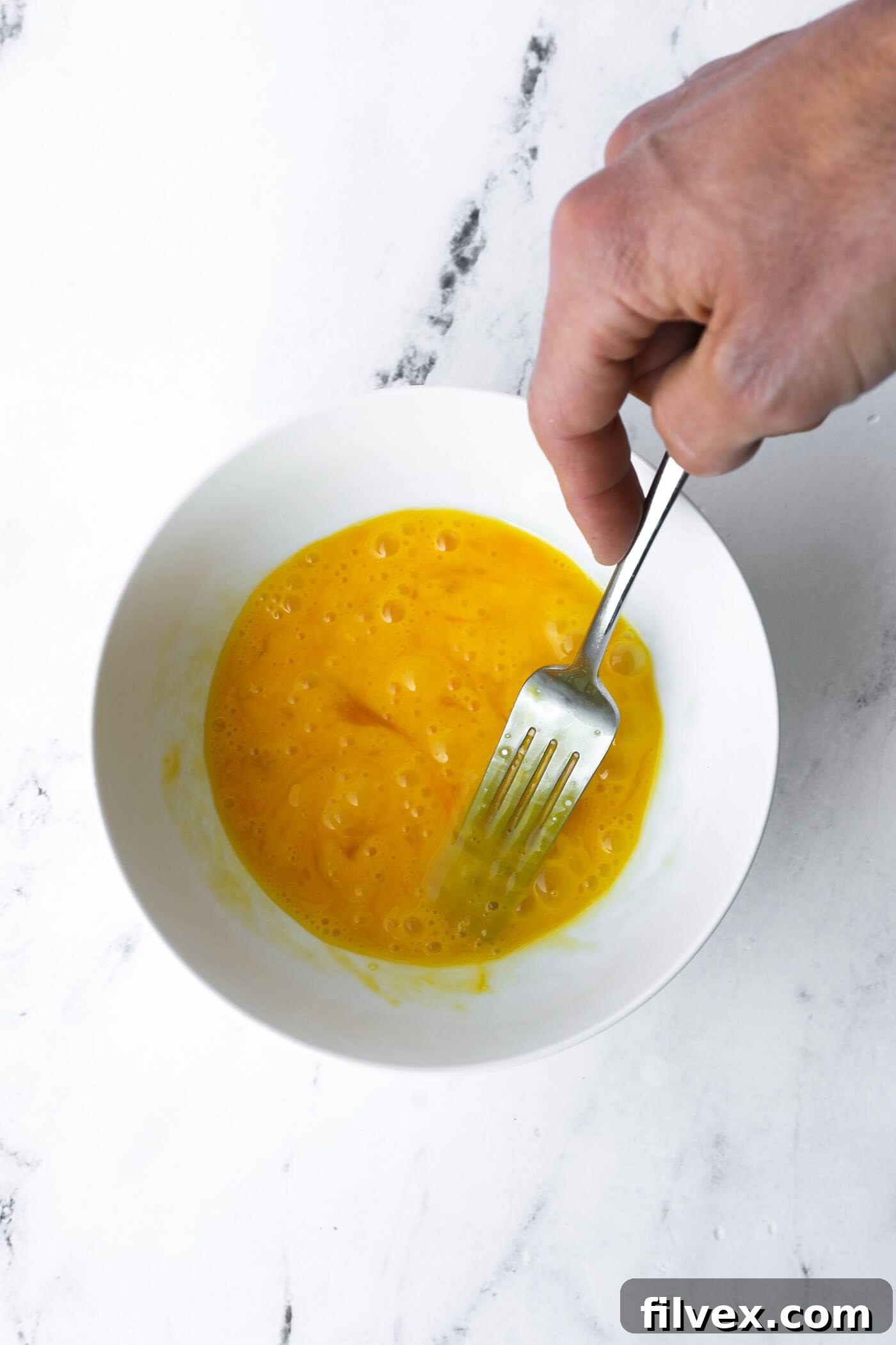 Eggs being whisked in a bowl, prepared for dipping chicken tenders.