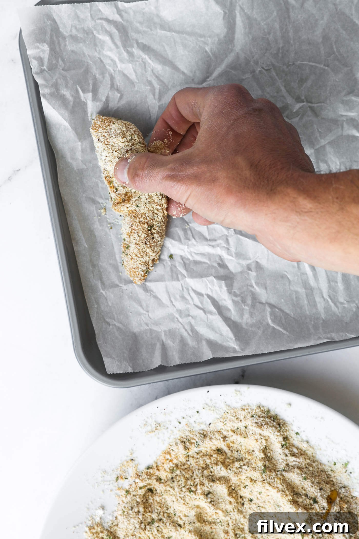 Coated chicken tenders placed on a parchment-lined baking sheet, ready for baking.