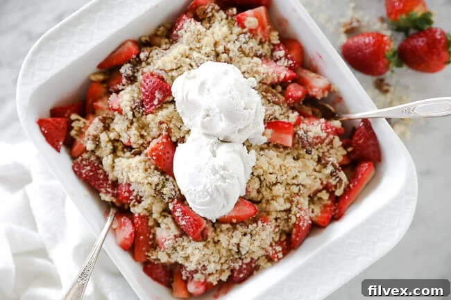 Horizontal overhead image of strawberry crumble in baking dish with two spoons dug in and two scoops of dairy-free ice cream on top.