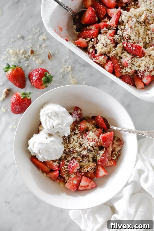 Vertical overhead image of strawberry crumble served up in a bowl with dairy-free ice cream on top and a spoon dug in.
