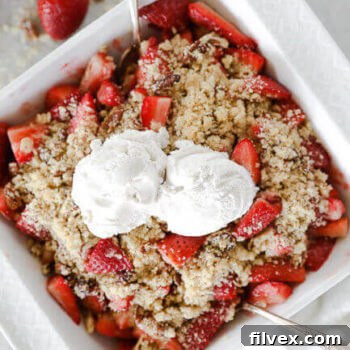 Fresh strawberry crumble in a dish with two scoops of vanilla ice cream on top