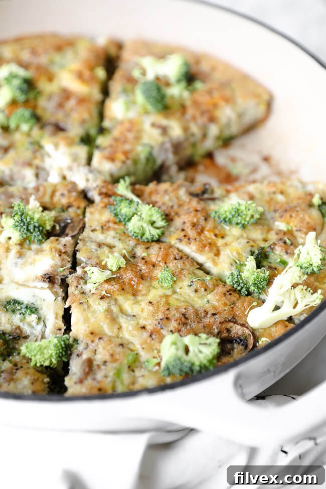 Vertical angled close up shot of Keto frittata in skillet with extra broccoli bits sprinkled on top.