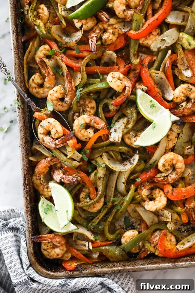sheet pan shrimp fajitas on a pan with onions, bell pepper and lime wedges overhead vertical image