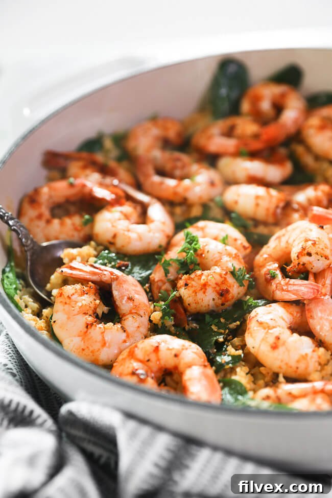 vertical angled close up image of cajun shrimp and cauliflower rice in skillet with a serving spoon. 