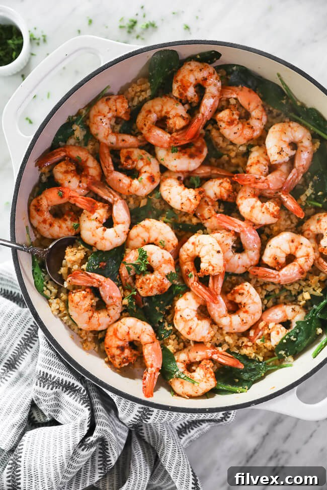 vertical overhead image of cajun shrimp and cauliflower rice in skillet with serving spoon. 