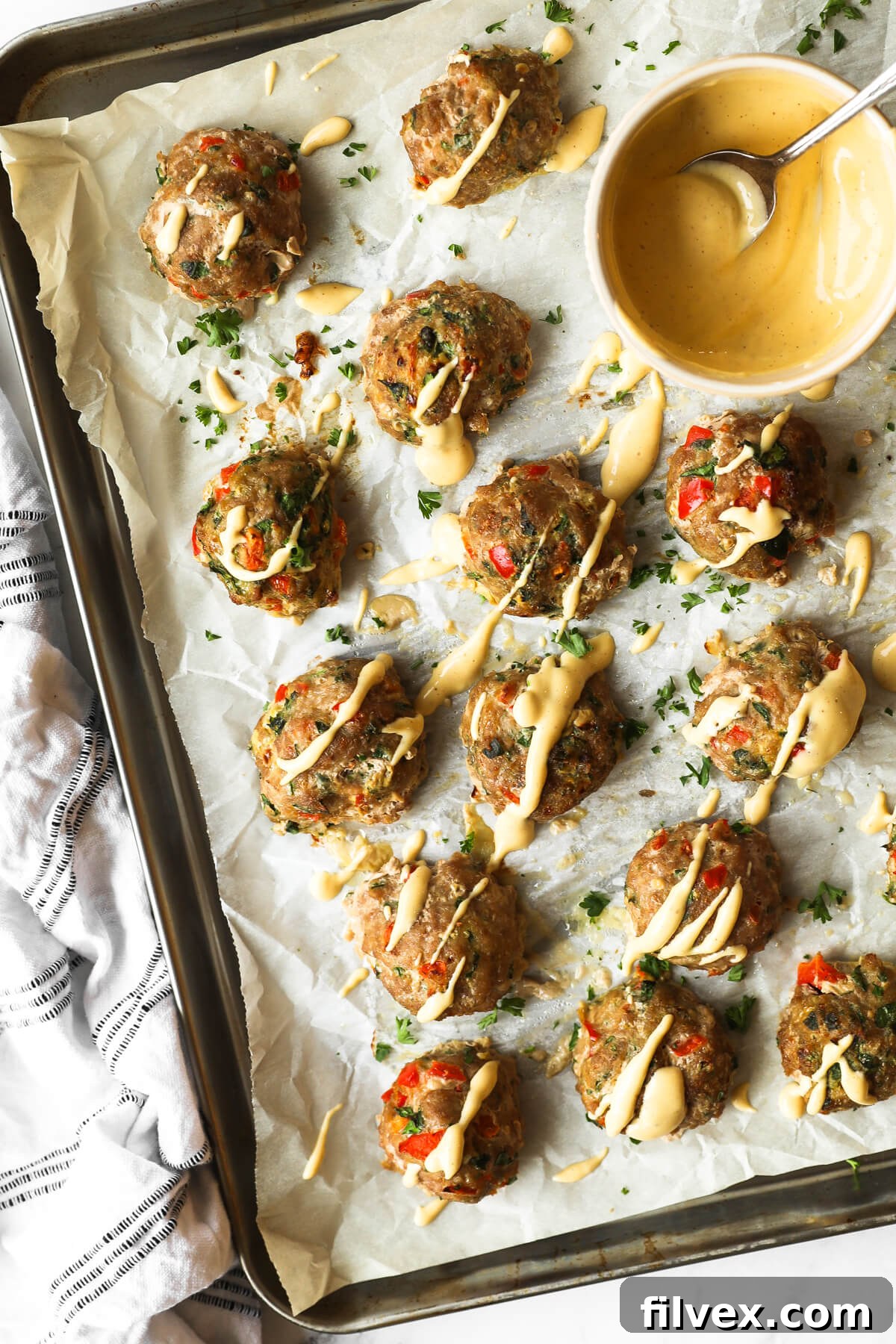 Overhead image of savory ground turkey meatballs arranged on a parchment-lined baking sheet, generously drizzled with a vibrant spicy sauce. A small ramekin of extra sauce sits nearby, ready for dipping.