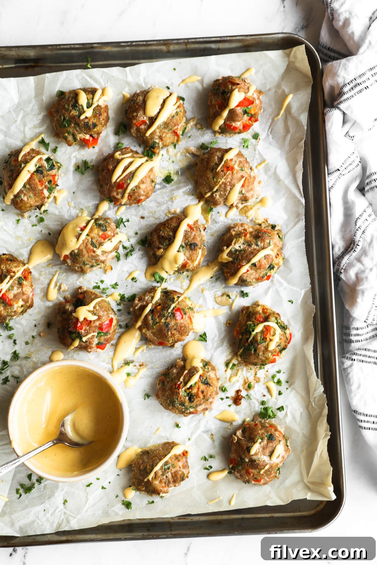 Overhead view of several perfectly baked turkey meatballs, golden-brown and glistening, arranged on a sheet pan. A generous dollop of creamy spicy aioli sauce is served on the side, ready for dipping.