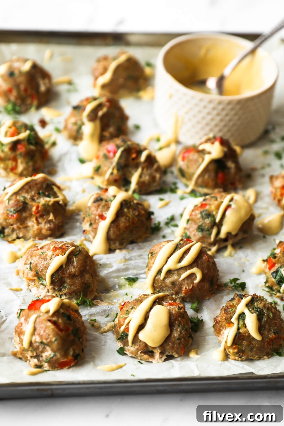 Angled close-up of tender keto turkey meatballs resting on a sheet pan, artfully garnished with a generous drizzle of spicy sauce. The front meatballs are in sharp focus, creating an enticing visual.
