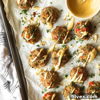 Overhead image of ground turkey meatballs on a sheet pan with spicy sauce drizzled on top. Extra sauce in a ramekin on the sheet pan.