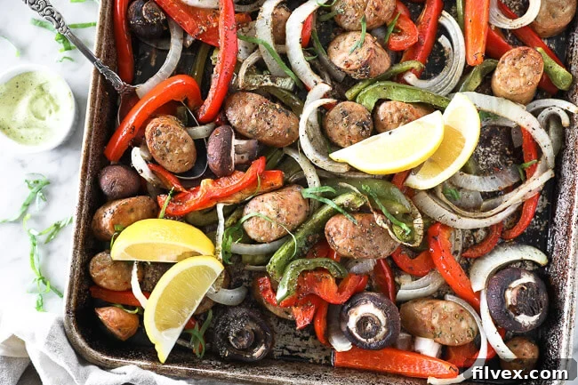 Horizontal overhead image of a sheet pan generously filled with perfectly roasted Italian sausage, colorful bell peppers, tender onion slices, and savory mushrooms. The dish is beautifully garnished with fresh basil leaves and bright lemon wedges, ready to be served.