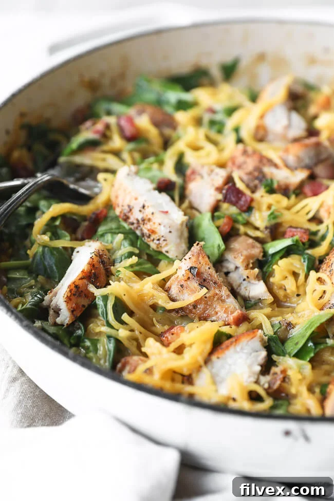 Vertical close up angled image of creamy spaghetti squash carbonara with chicken and bacon in a skillet, ready to be served. 