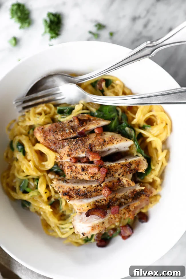 Vertical close up image of spaghetti squash carbonara served in a white bowl with a fork and spoon, topped with extra crispy bacon bits and fresh chopped parsley for garnish. 