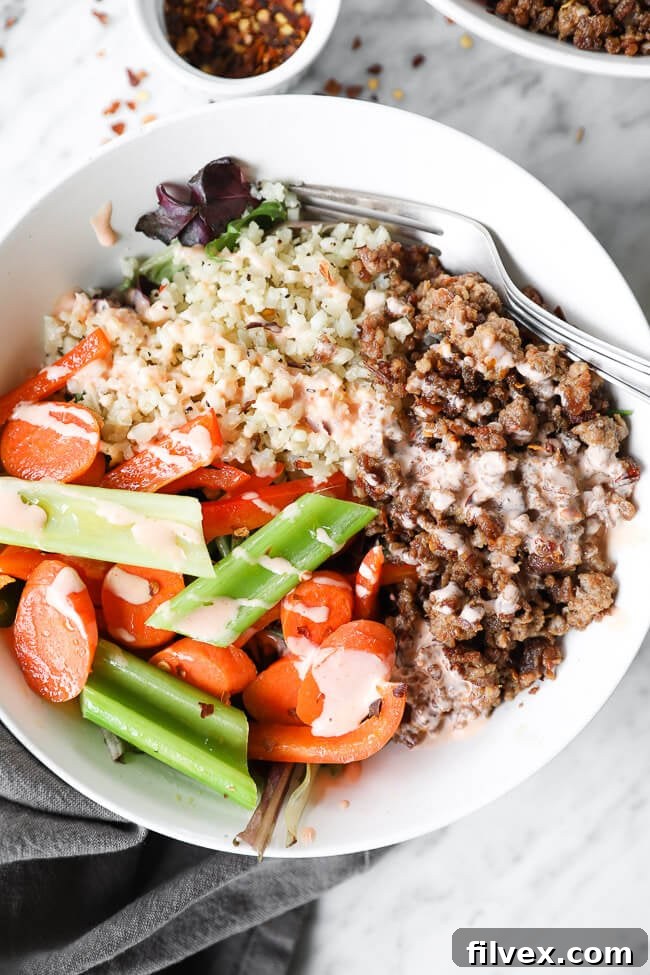 Vertical overhead close up image of a spicy pork bowl with cauliflower rice, pork, veggies and spicy sauce drizzled on top, ready to be enjoyed.
