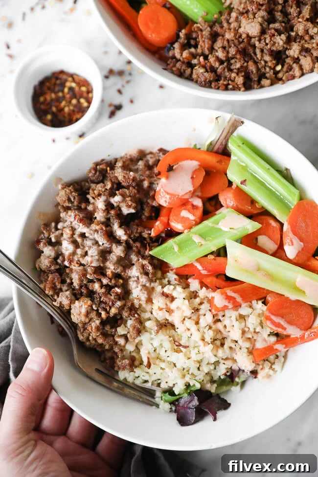 Overhead close up image of hands holding a bowl of spicy pork, cauliflower rice and veggies, with a clear focus on the delicious ingredients.