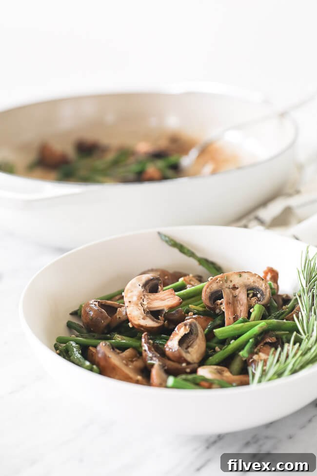 A close-up shot of the cooked garlicky mushrooms and asparagus with fresh rosemary garnish