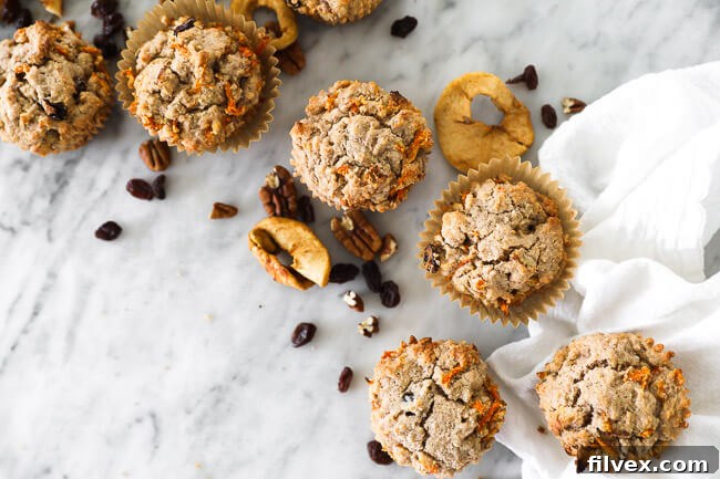 Horizontal overhead image of morning glory breakfast muffins spread out on marble with dried apples, raisins and pecans sprinkled around. Delicious Paleo and Vegan muffins, perfect for a healthy breakfast.