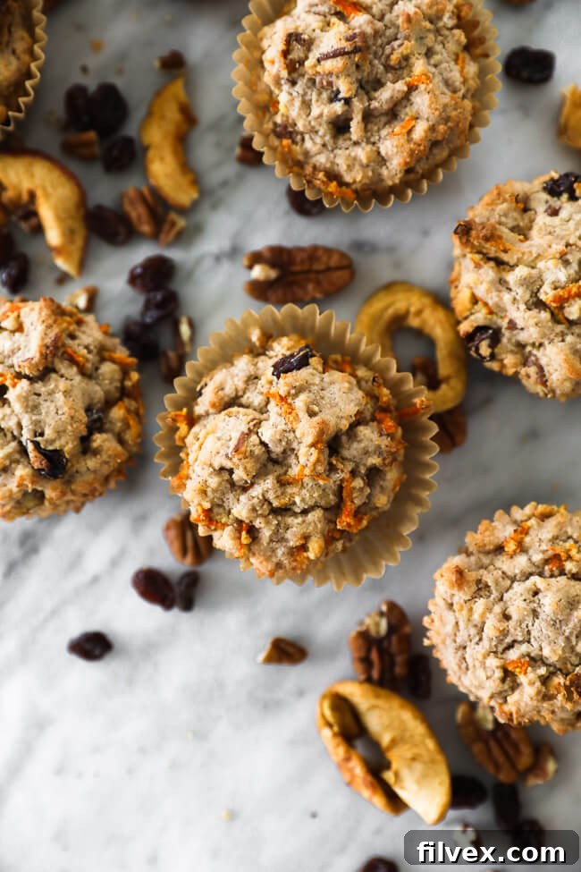 Vertical overhead close up of morning glory breakfast muffins on marble with pecans, dried and raisins sprinkled around. Hearty Paleo and Vegan muffins.
