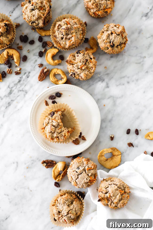Overhead vertical image of paleo breakfast muffins on marble with one muffin a plate with a bite taken out. Enjoying a nutritious Morning Glory Muffin.