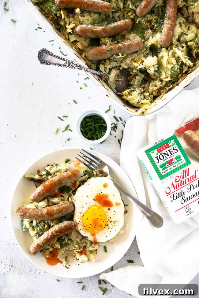 Vertical overhead image of breakfast casserole served up on a plate with sausages and a fried egg on top. 