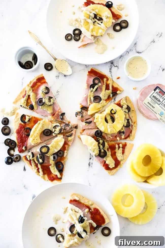 vertical overhead image of hawaiian pizza cut into slices on marble and then served up on two plates with extra dairy free sauce drizzled on top.