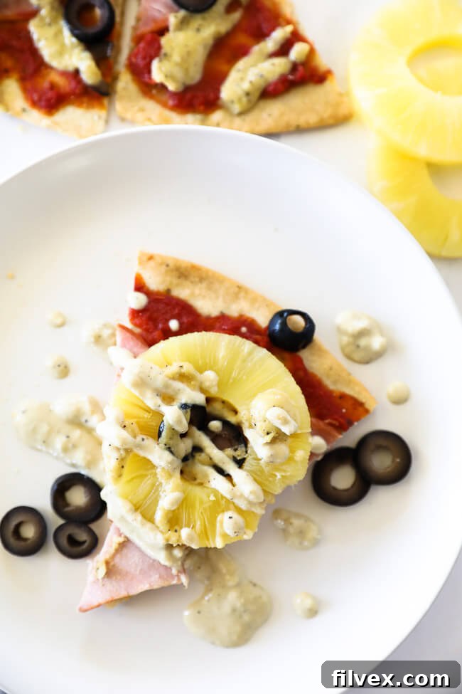 Vertical overhead image of a single slice of paleo hawaiian pizza served on a plate with extra dairy free sauce drizzled on top.