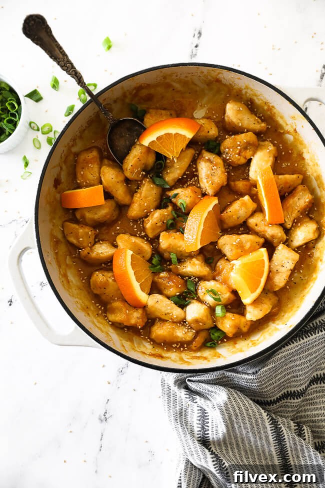 Healthy orange chicken in pan with orange slices and spoon vertical image.