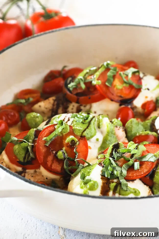 Vertical angled image of chicken caprese in skillet. Chicken breasts topped with mozzarella cheese, tomatoes, pesto, balsamic and fresh basil. 