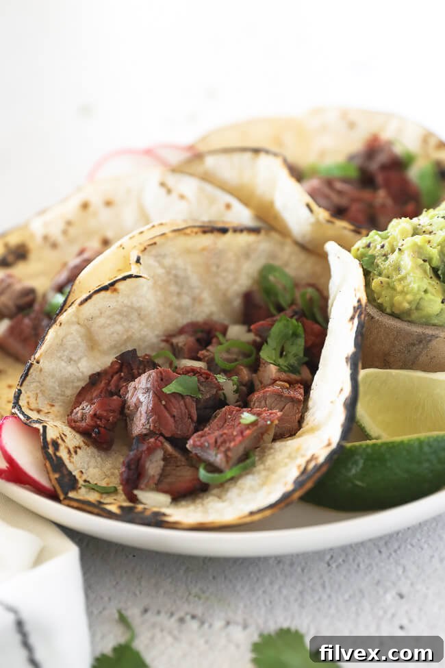 Three delicious Carne Asada tacos on a plate, garnished with fresh cilantro, thinly sliced radishes, and diced white onion. A close-up angle showcasing the vibrant colors and appealing presentation.